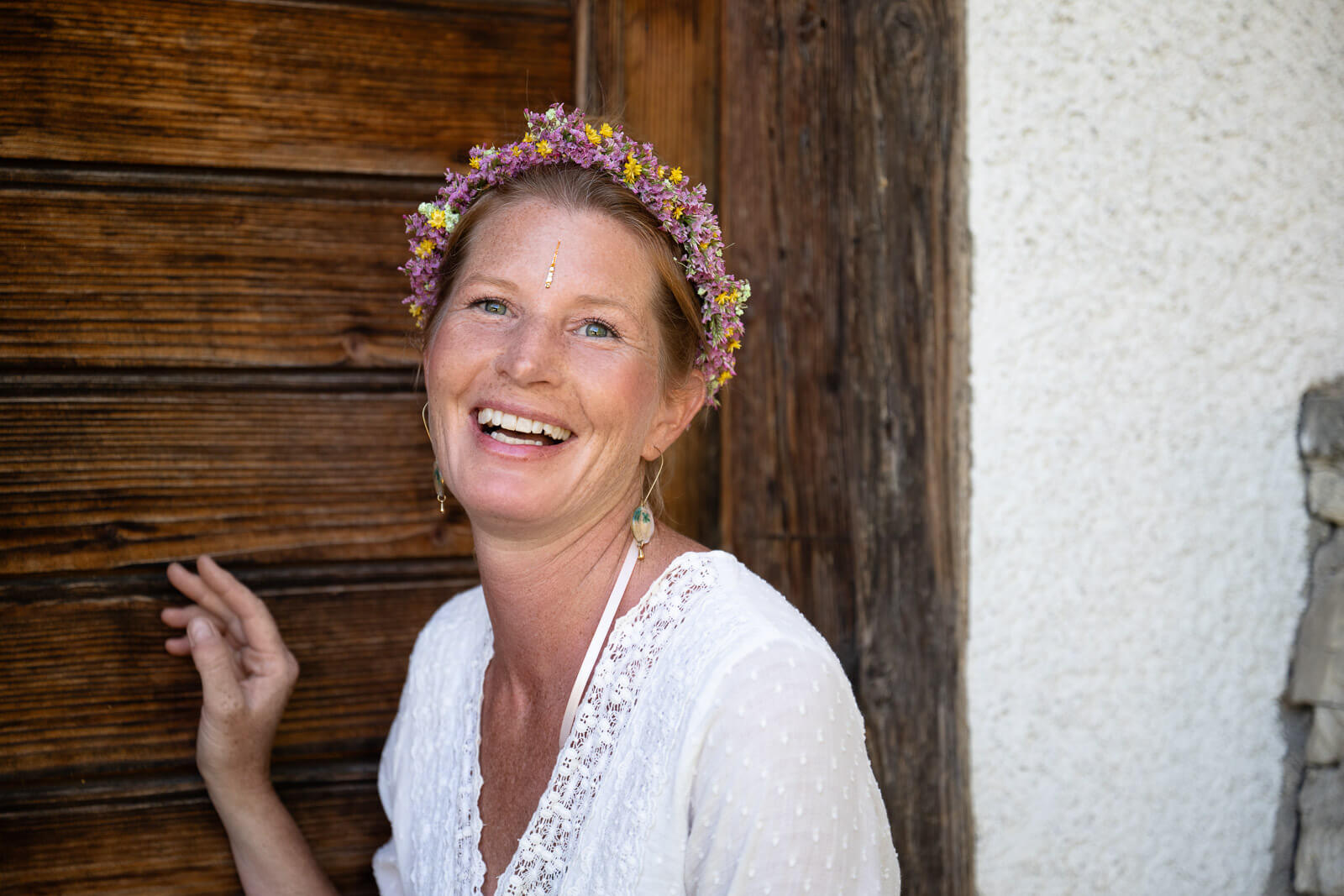 Portraitaufnahme von Sybille Jeanne Buntschu mit Blumenkranz, lachend vor einer Holzwand